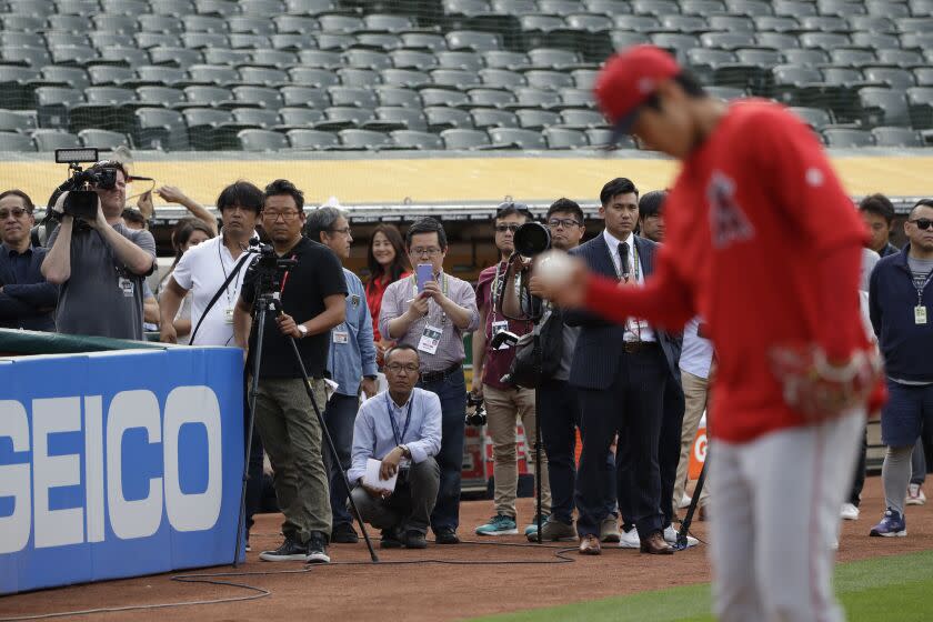 A group of media members watch Los Angeles Angels pitcher Shohei Ohtani, right, throw a bullpen session.
