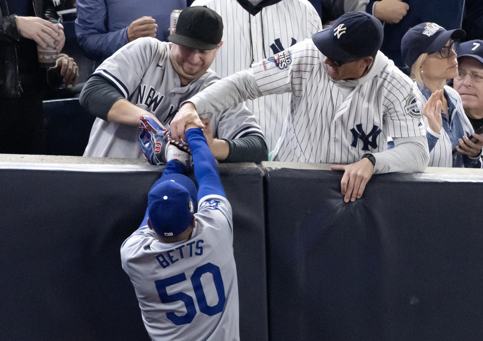 NEW YORK, NEW YORK - OCTOBER 29: Fans Austin Capobianco (L) and John Peter (R) interfere with Mookie Betts #50 of the Los Angeles Dodgers as he attempts to catch a fly ball in foul territory during the first inning of Game Four of the 2024 World Series against the New York Yankees at Yankee Stadium on October 29, 2024 in the Bronx borough of New York City. The play resulted in an out.  (Photo by Al Bello/Getty Images)